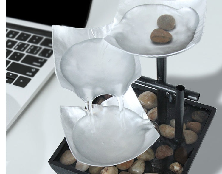 Decorative water fountain with stones on a desk next to a laptop