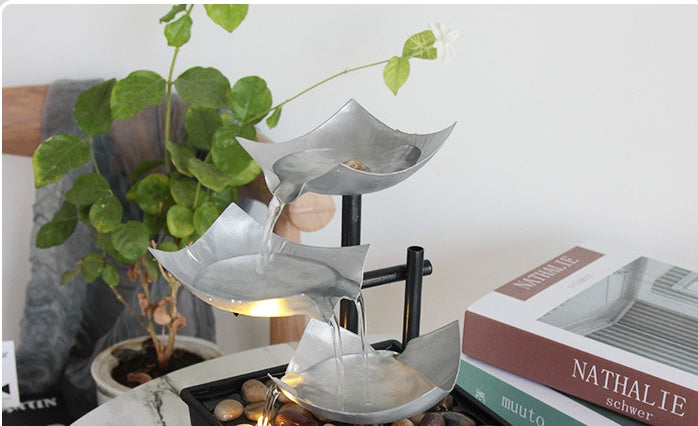 Metallic water fountain with a plant and books in the background